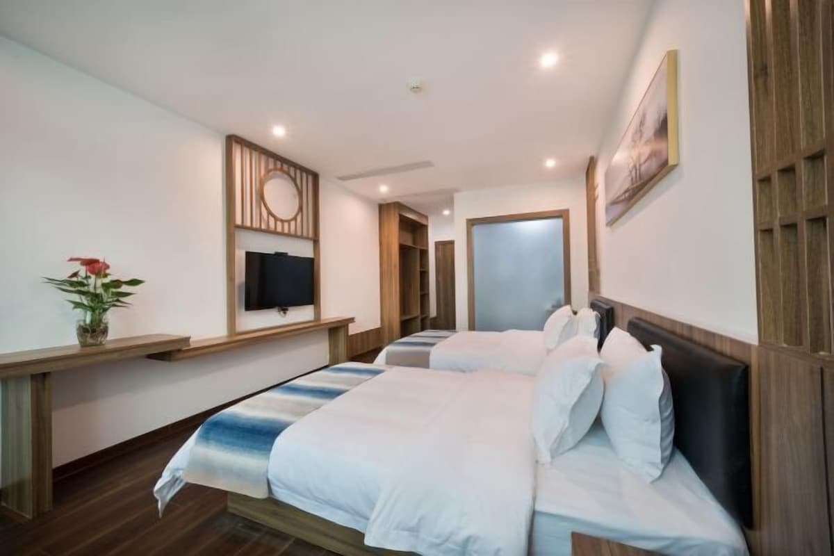 A hotel room with two beds, a TV, a wooden shelf, and a painting on the wall.