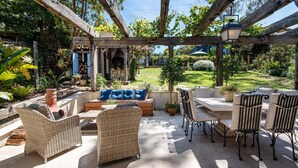 An outdoor patio with wicker furniture, a stone fireplace, and a view of a lush garden. - Pet Friendly - Chateau Rouge - Provincial Home Red Hill (Red Hill)
