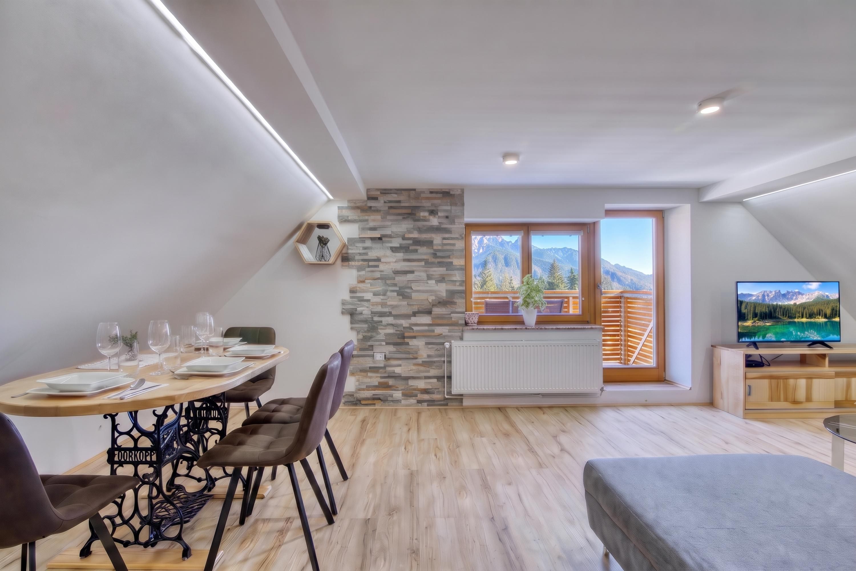 Een eetgedeelte met een tafel voor vier personen, een bank en een televisie in een kamer met uitzicht op de bergen.