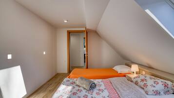 A bedroom with two beds, a wooden floor, a skylight, and a small bedside table with a lamp.