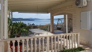 Un espacio al aire libre cubierto con vista al mar, una mesa, sillas y plantas en macetas.