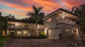 A two-story house with a garage, surrounded by palm trees and a brick driveway. - Ponderosa, a gorgeous and spacious five bedroom beach house (Blueys Beach)