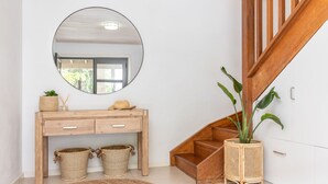 A modern interior with a wooden console desk, a round mirror, wicker baskets, a staircase, and a potted plant. - Ponderosa, a gorgeous and spacious five bedroom beach house (Blueys Beach)