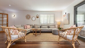 A living room with a sectional sofa, two wicker chairs, a coffee table, and a floor lamp. - Ponderosa, a gorgeous and spacious five bedroom beach house (Blueys Beach)