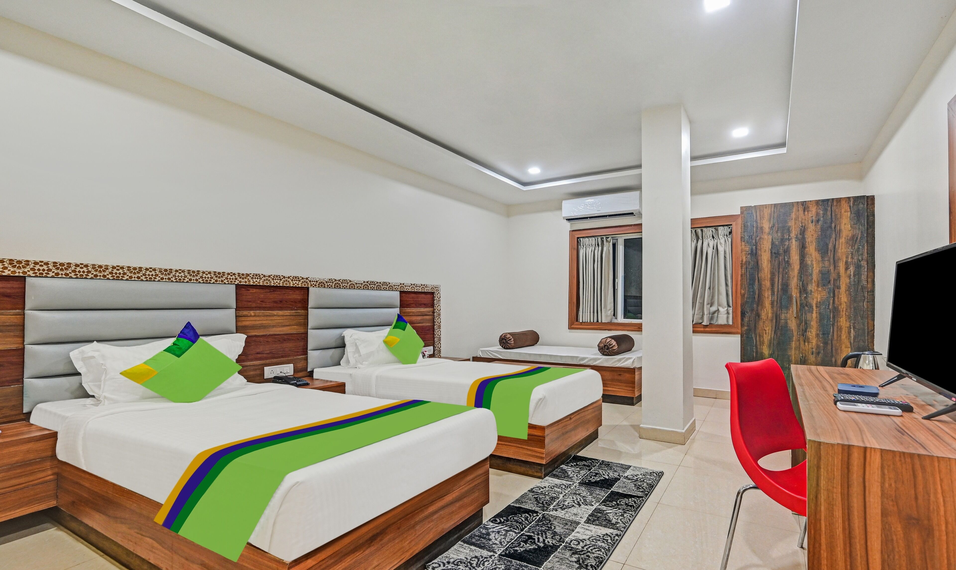 A hotel room with two beds, a desk, a chair, a TV, and a window with curtains.