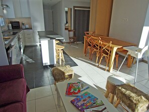 A modern kitchen with white cabinets, a dining area with wooden chairs, and a white table with children's books.