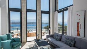 Un vaste salon doté de grandes fenêtres offrant une vue sur la mer et les montagnes.