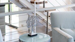 Un intérieur moderne avec un escalier, une table ronde en verre surmontée d’une sculpture en métal, et deux fauteuils bleu clair.