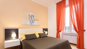 A bedroom with a bed, nightstands, a painting, and orange curtains. - Appartamento Vaticano per 6 persone (Rome)