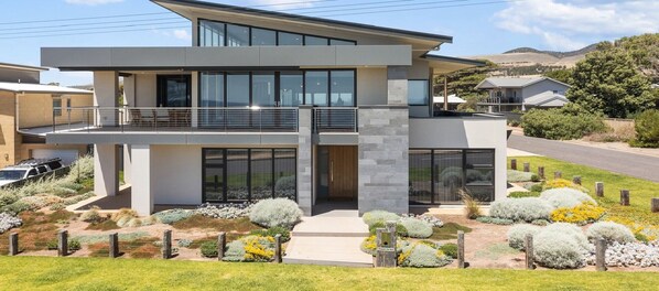 A modern two-story house with a balcony, large windows, and a landscaped garden.
