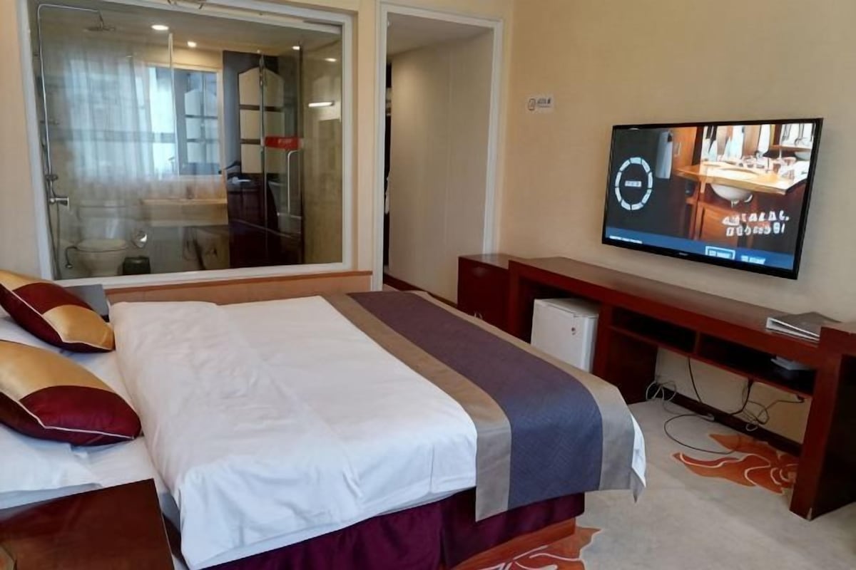 Una habitación de hotel con una cama, televisión, escritorio y espejo.