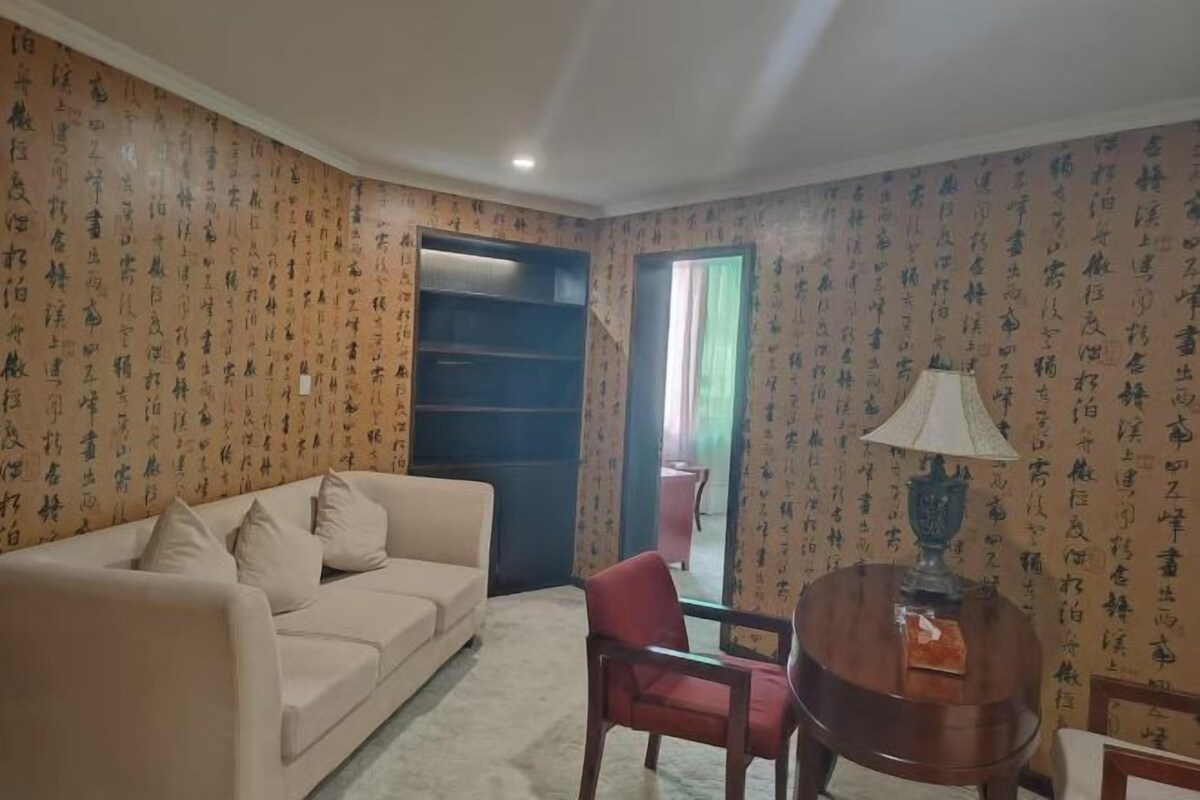 A living room with a sofa, a red chair, a small table with a lamp, and a bookshelf.