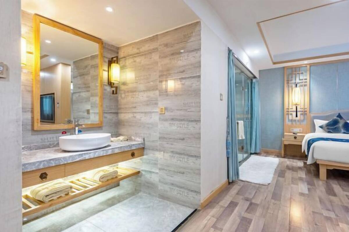 Ein modernes Hotelzimmer mit Marmorbad, einem großen Spiegel, einem Bett mit blauer Bettwäsche und Holzboden.