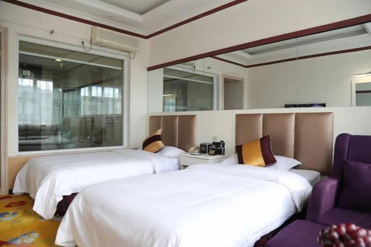 Ein Hotelzimmer mit zwei Betten, einem Nachttisch, einem violetten Sessel und einem großen Fenster.