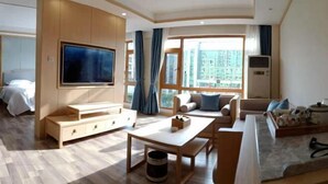 A modern living room with a flat-screen TV, wooden furniture, a sofa set, and large windows offering a city view. - Jinmeng Hotel (Wenshan City)
