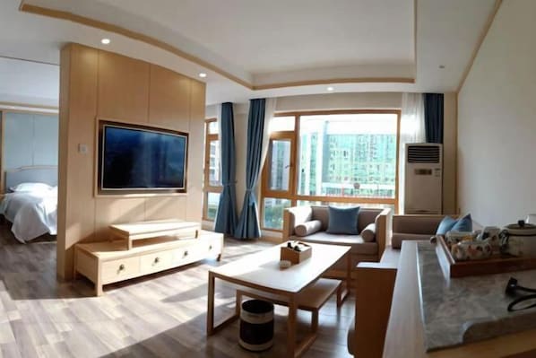 Un salón moderno con televisión de pantalla plana, muebles de madera, un conjunto de sofás y ventanas amplias con vistas a la ciudad.