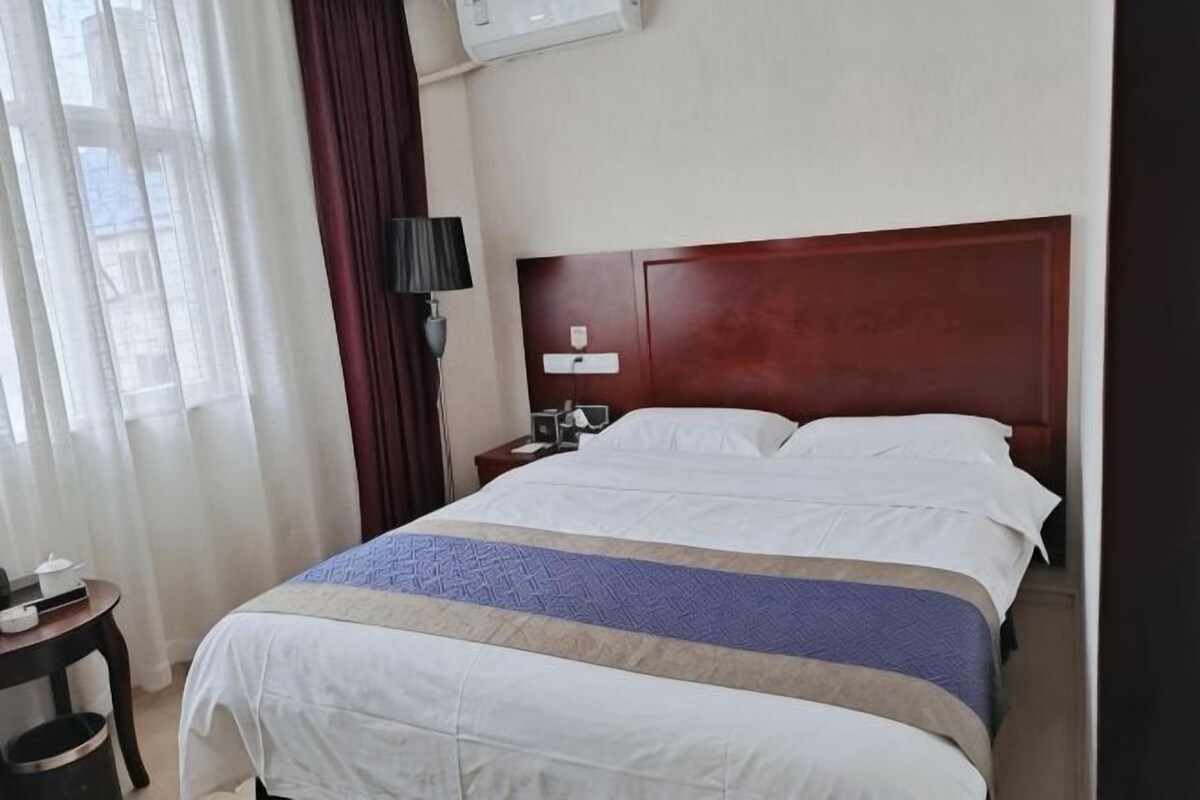 Una habitación de hotel con una cama grande, una mesita de noche, una lámpara y una ventana con cortinas.