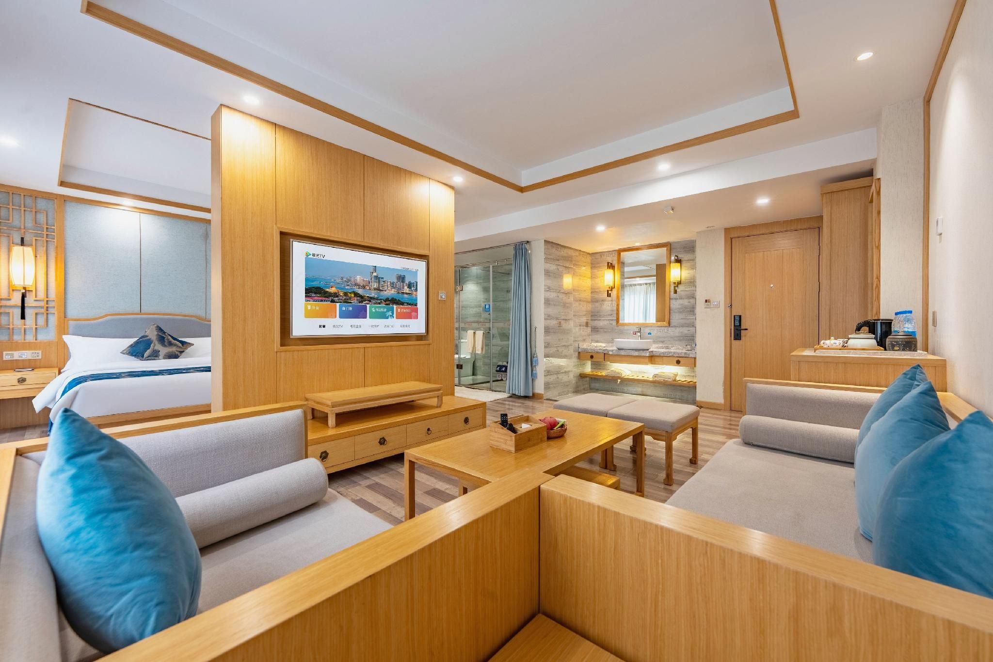A modern hotel room with a TV, sofa, coffee table, and a bathroom with a shower and sink.