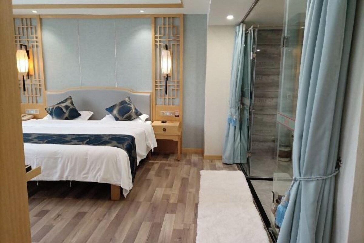 A hotel room with two beds, a wooden headboard, bedside lamps, a nightstand, a glass shower, and a curtain.