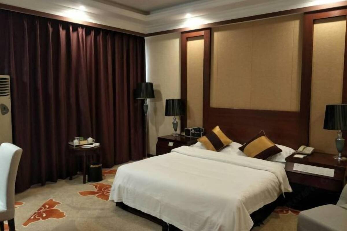 Ein Hotelzimmer mit einem großen Bett, zwei Nachttischen, einem Sessel, einem Schreibtisch, einer Lampe und einem Vorhang.