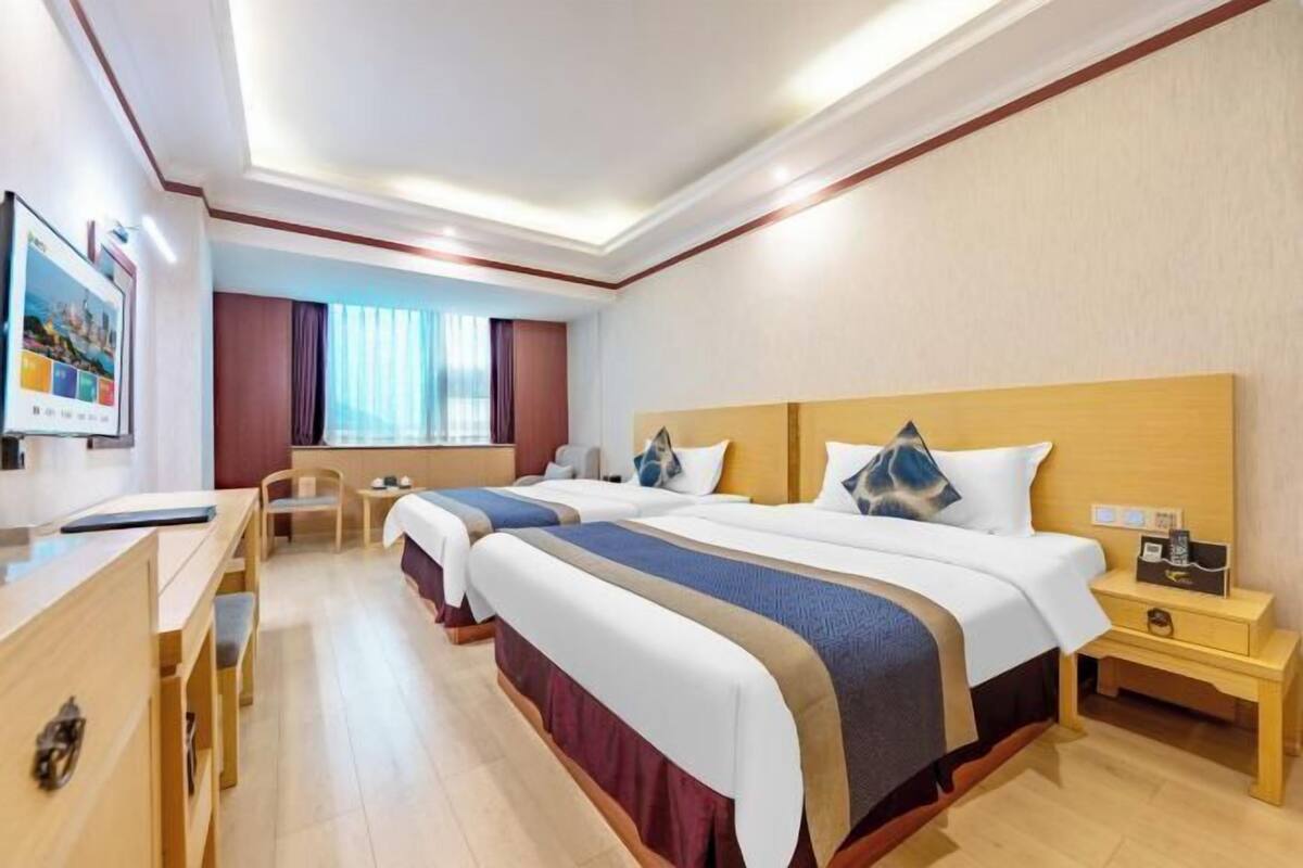Ein Hotelzimmer mit zwei Betten, einem Schreibtisch, einem Stuhl, einem Nachttisch und einem Fenster mit Vorhängen.