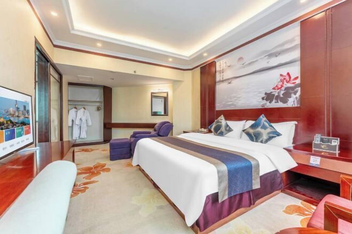 Ein Hotelzimmer mit einem großen Bett, einem Fernseher, einem Schreibtisch und einem Gemälde an der Wand.