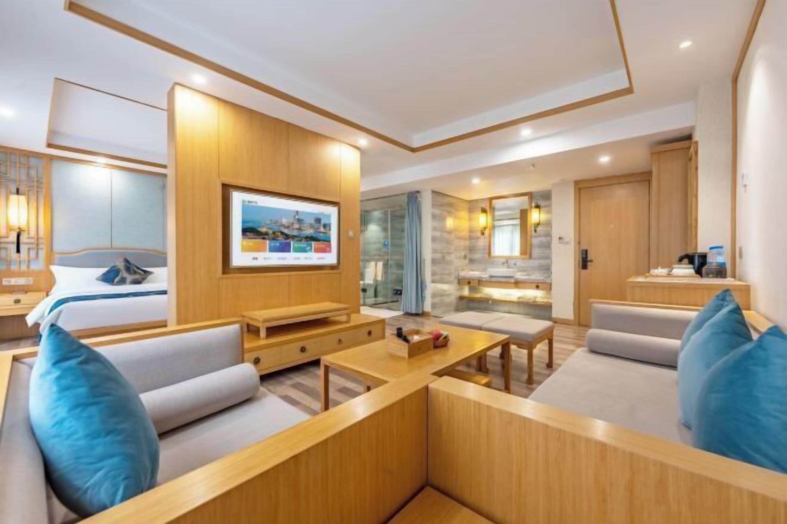 Une chambre d’hôtel moderne dotée d’un grand lit, d’un téléviseur fixé au mur, d’un coin salon avec une table basse et d’une petite kitchenette.