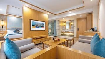 A modern hotel room with a large bed, a TV mounted on the wall, a seating area with a coffee table, and a small kitchenette.