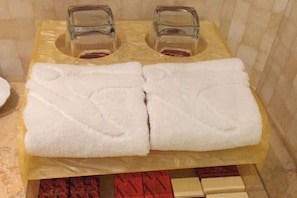 Un baño con dos lavamanos, cada uno con un vaso sobre el mostrador, y dos toallas blancas dobladas en un toallero amarillo.