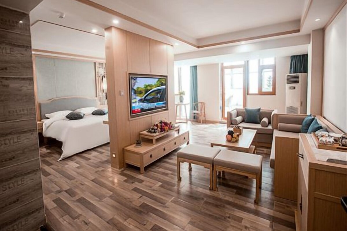 A modern hotel room with a bed, a TV, a sofa, a coffee table, and a dining area.
