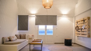 A modern living room with a sofa, a small table, a round rug, a wall-mounted light fixture, and a view of the sea through a window.