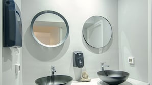 A modern bathroom with two round mirrors, a black vessel sink, and a white countertop.