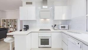 Een moderne keuken met witte kastjes, een ingebouwde oven, een magnetron en een koffiezetapparaat.
