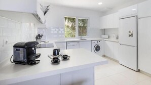 Een moderne keuken met witte kastjes, een koffiezetapparaat, een wasmachine en een koelkast.