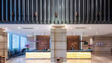 A modern hotel lobby with two reception desks, large windows, and a high ceiling with vertical panels.