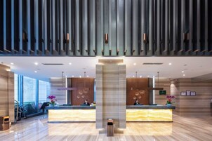 Un moderno vestíbulo de hotel con dos mostradores de recepción, ventanas amplias y un techo alto con paneles verticales.