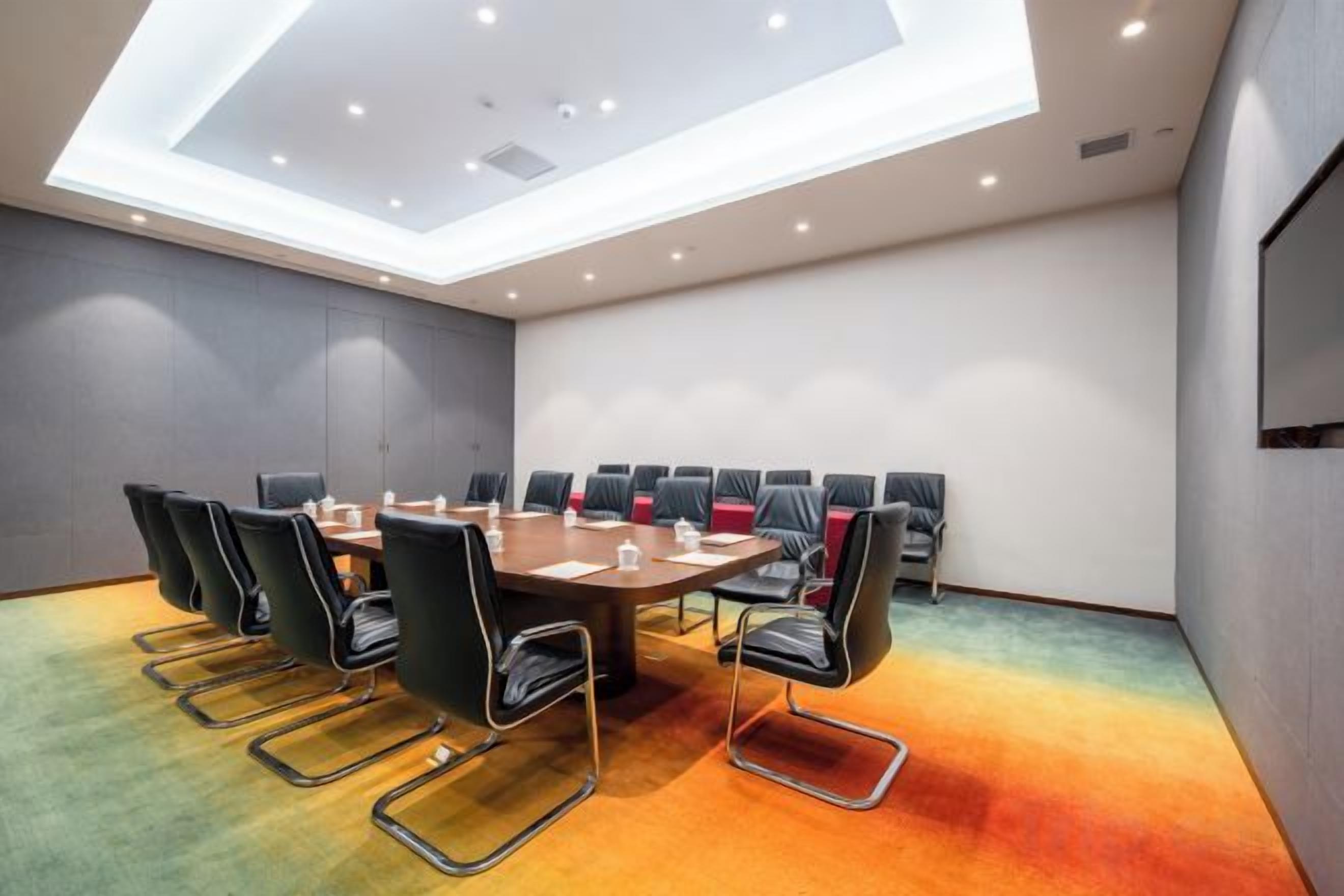 A conference room with a high ceiling, a large table, and multiple chairs.