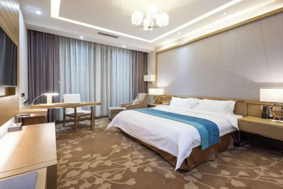 Hotellihuone, jossa on suuri sänky, työpöytä, tuoli ja työpöytälamppu.