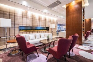 A modern hotel lobby with a sofa, red chairs, a coffee table, and a fireplace. - Golden Sun Hotel (Lai'an)