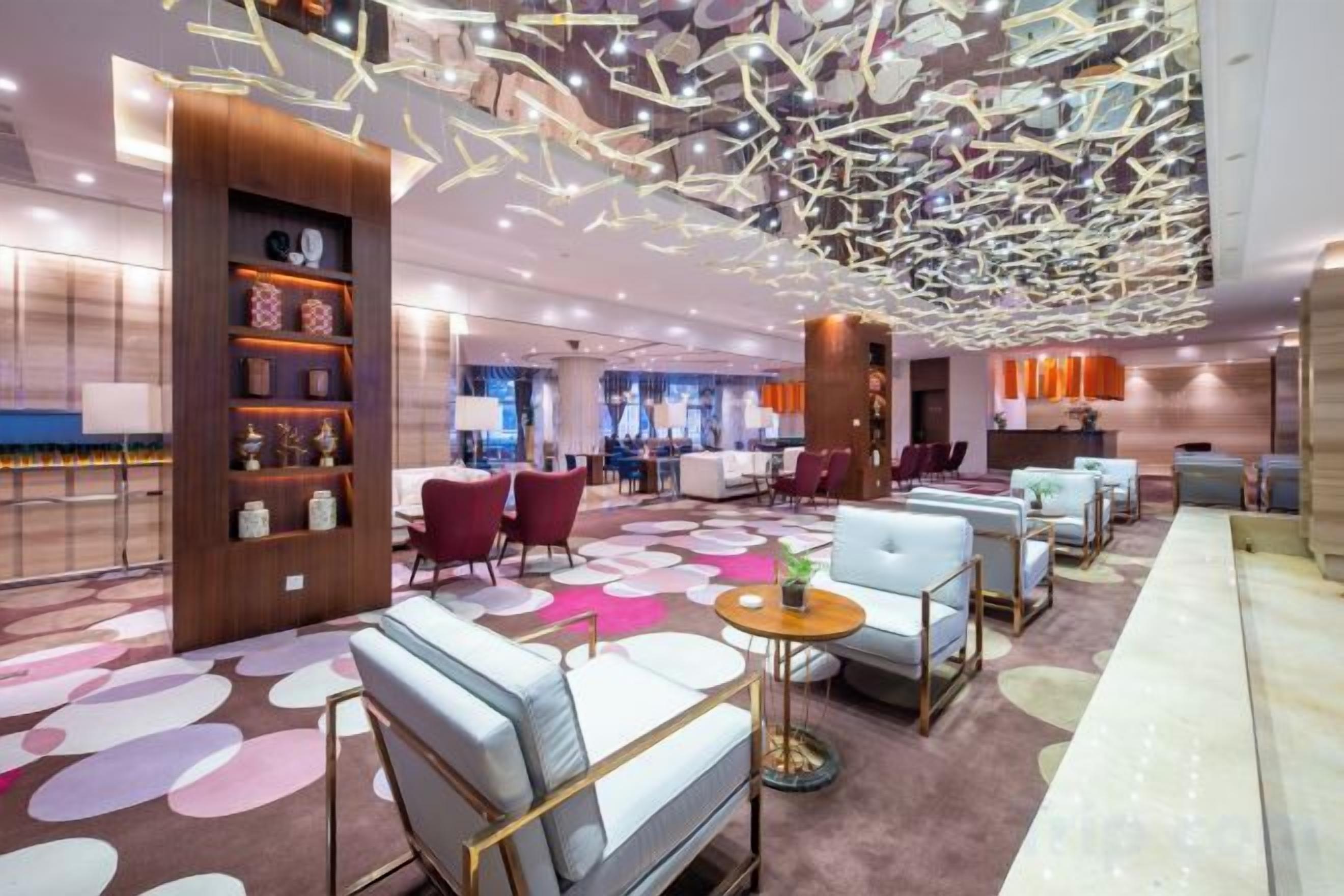 A modern hotel lobby with seating areas, a reception desk, and a bar.