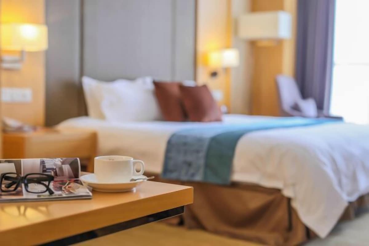 Una habitación de hotel con una cama, una mesita de noche con una taza y vasos, y una revista.