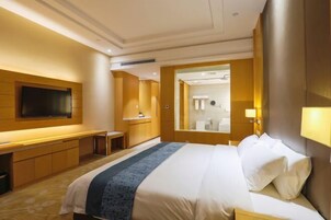 Habitación de hotel con una cama grande, un escritorio, televisión y un baño visible a través de una puerta abierta.