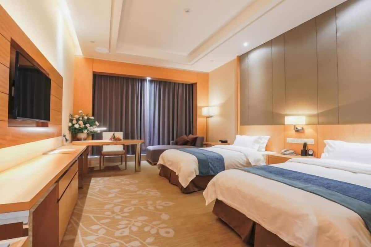 Hotellihuone, jossa on kaksi sänkyä, työpöytä, tuoli, televisio ja suuri ikkuna, jossa on verhot.