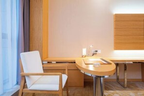 Una habitación de hotel moderna con un escritorio de madera, una silla blanca y un ventanal con cortinas.