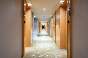 A hotel corridor with wooden doors, a carpeted floor, and a ceiling with recessed lighting. - Golden Sun Hotel (Lai'an)