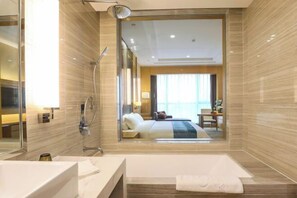 Habitación de hotel moderna con un espejo grande, cabina de ducha, baño separado, cama con vistas y zona de comedor.