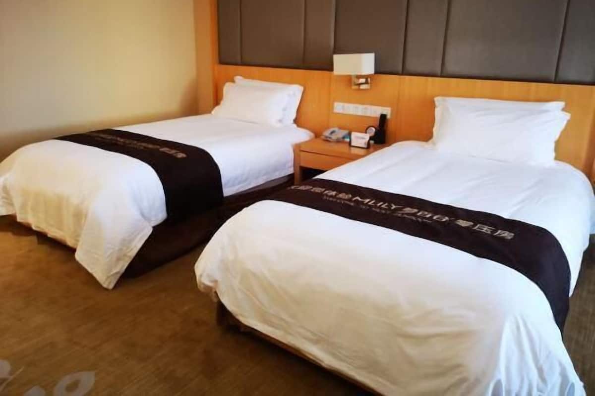 Hotellihuone, jossa on kaksi sänkyä, yöpöytä, jossa on puhelin ja lamppu, sekä puinen pääty.