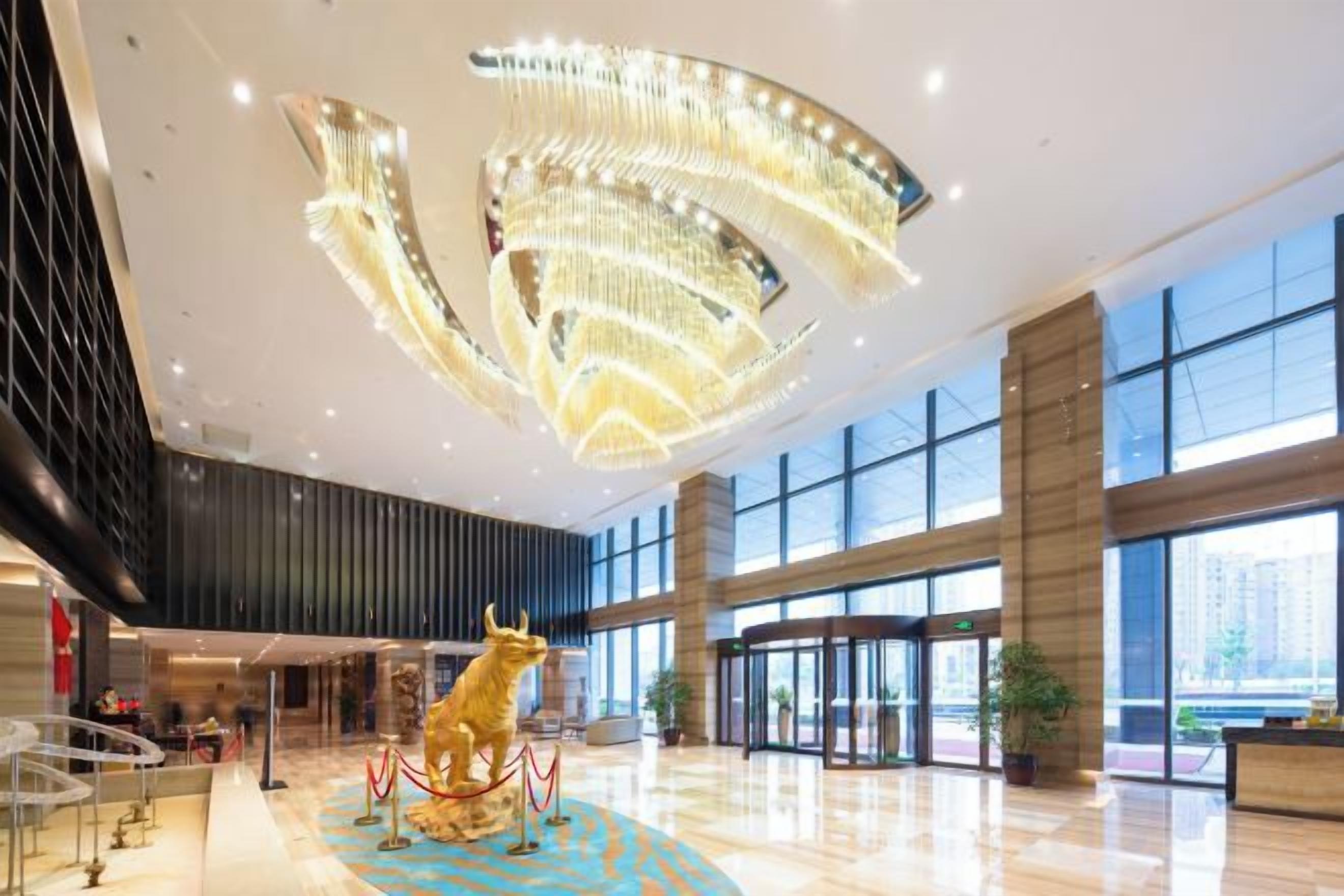 A spacious lobby with a modern chandelier, a bull sculpture, and large windows.