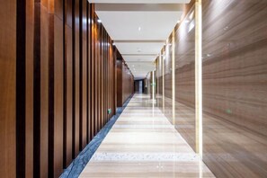 A corridor with wooden paneling on one side and a reflective floor, leading to a door at the end. - Golden Sun Hotel (Lai'an)