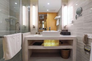 Un baño moderno con cabina de ducha de vidrio, tocador con lavamanos, espejo y perchero.